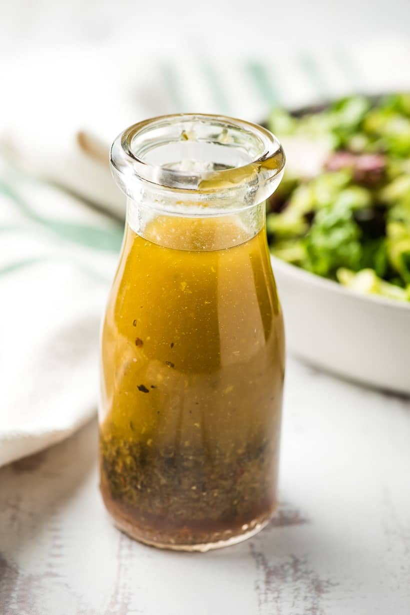 bottle of homemade italian dressing with salad in the background