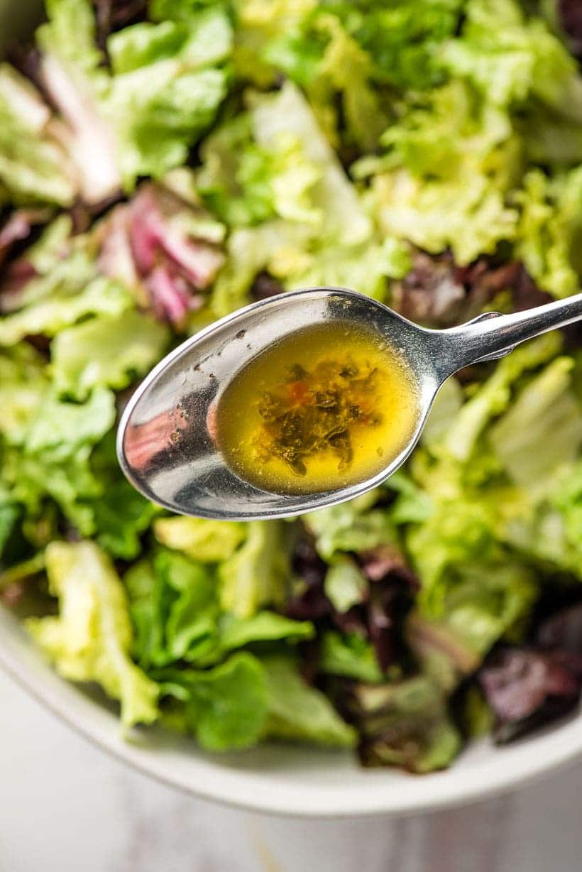 spoon holding homemade Italian dressing over salad greens
