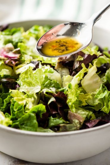 spoonful of Italian dressing recipe drizzling over salad greens