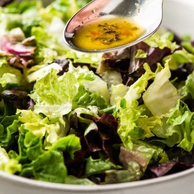spoonful of Italian dressing recipe drizzling over salad greens