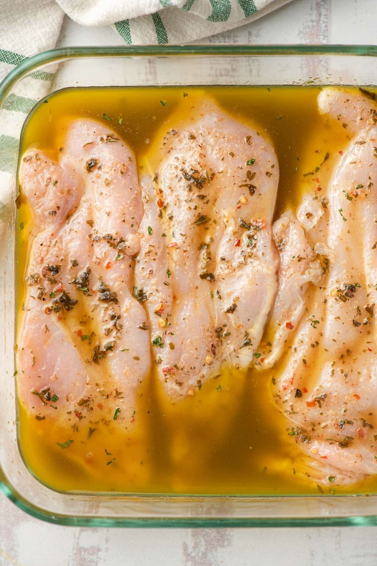 Raw chicken marinated in Italian dressing in a baking dish.