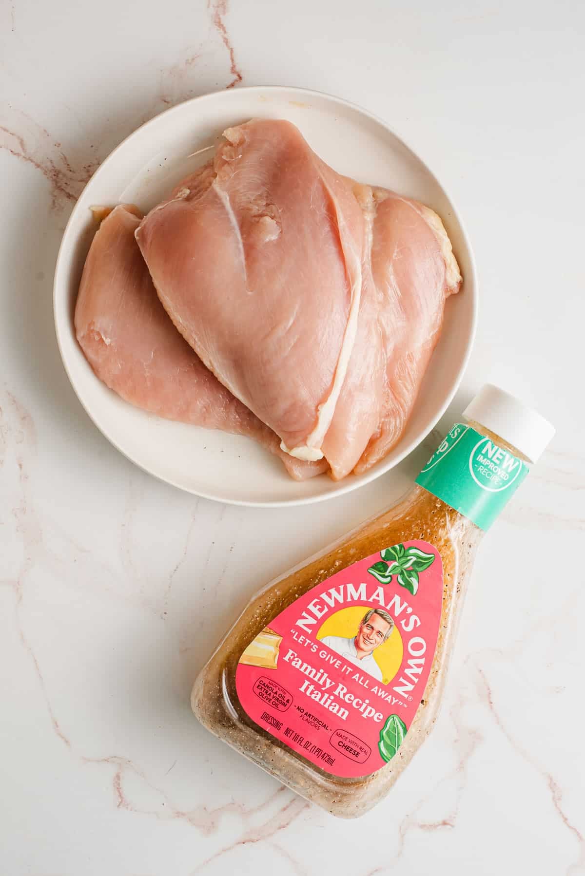 A plate of chicken breasts and bottle of Italian dressing.