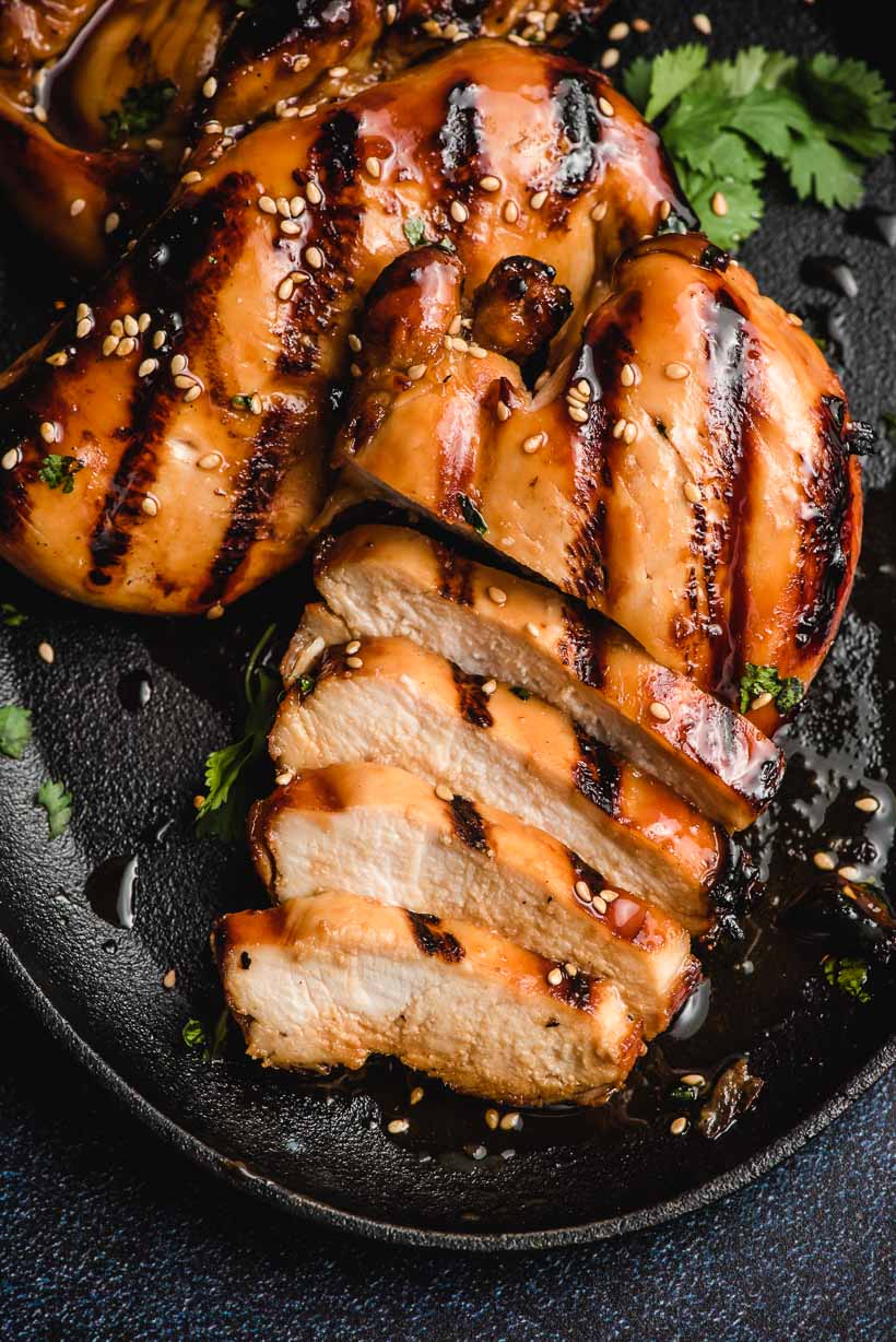 slices of grilled Asian chicken breast on a skillet coated in a sweet glaze sauce