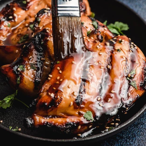 Soy sauce and honey glaze being brushed on grilled chicken.