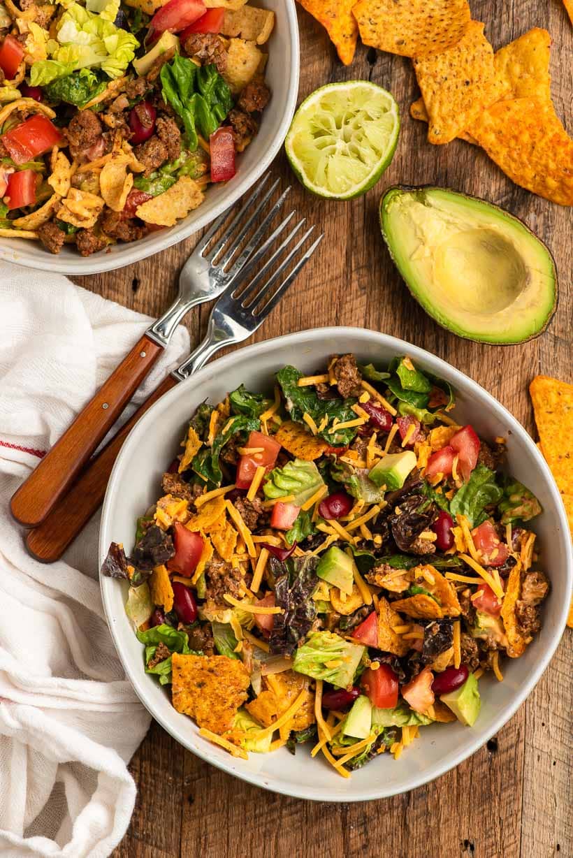 bowl of doritos taco salad served with fresh avocado on a table with napkin and fork