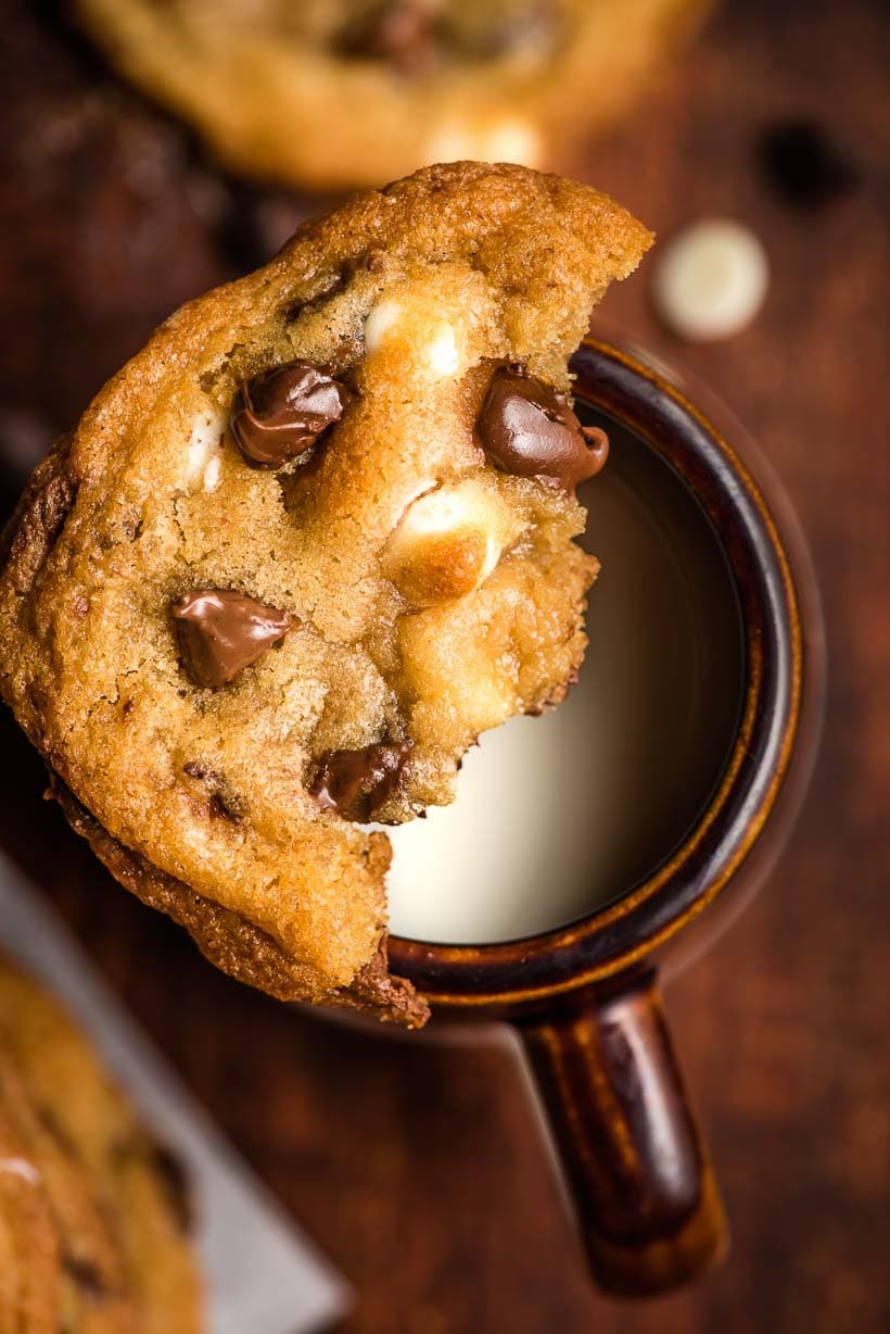 half of a chocolate chip cookie balanced on a mug of milk