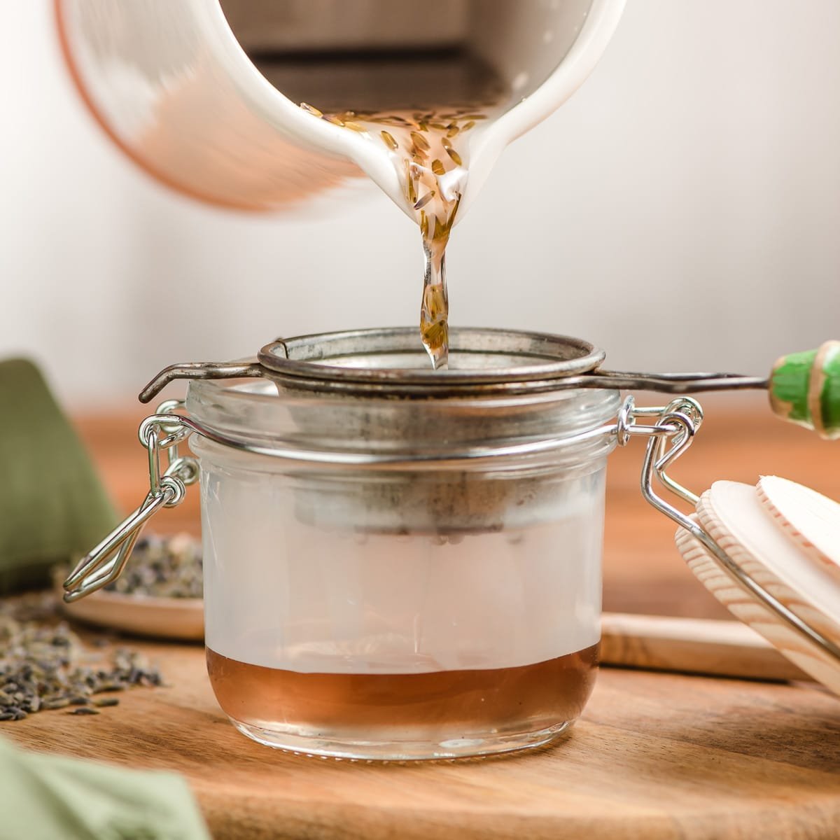 Lavender simple syrup being poured through a strainer into a jar.