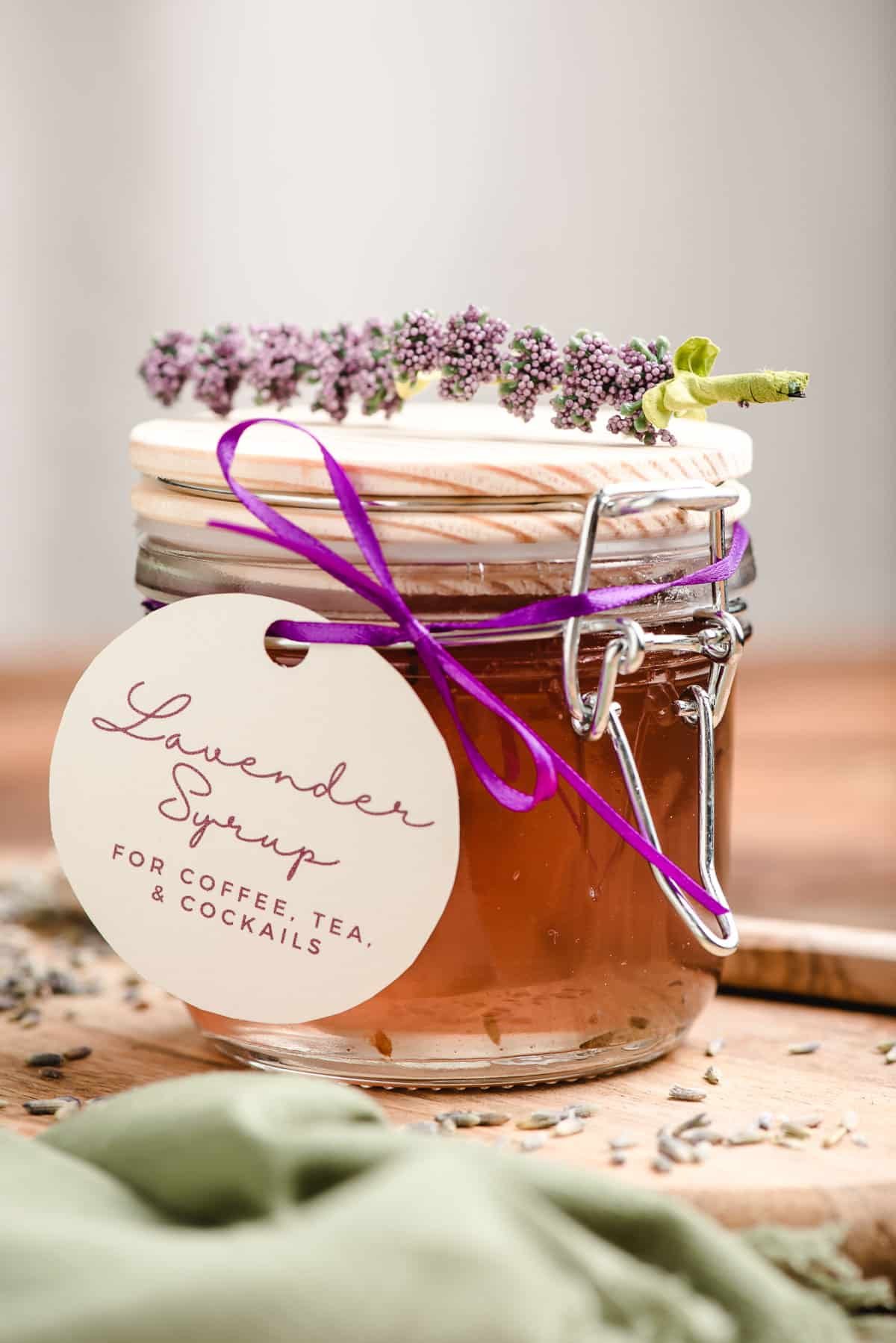 Lavender syrup in a glass jar with a homemade tag tied on with a ribbon.