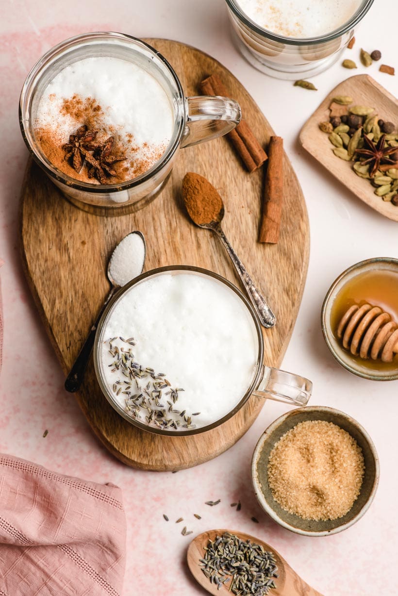 tea lattes on a wood tray with bowls of sugar, honey, and lavender buds around