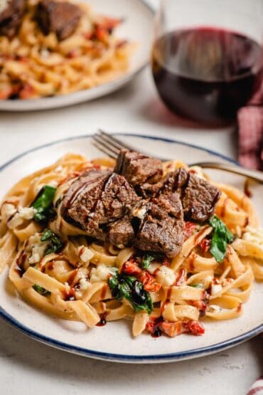 Steak pasta with spinach and sundried tomatoeson a white plate