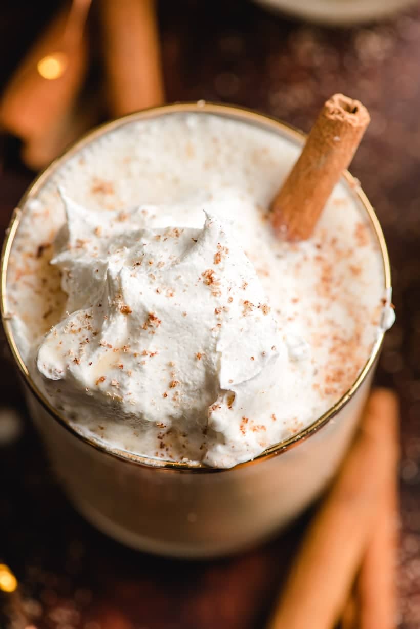 eggnog in a glass with whipped cream and cinnamon stick