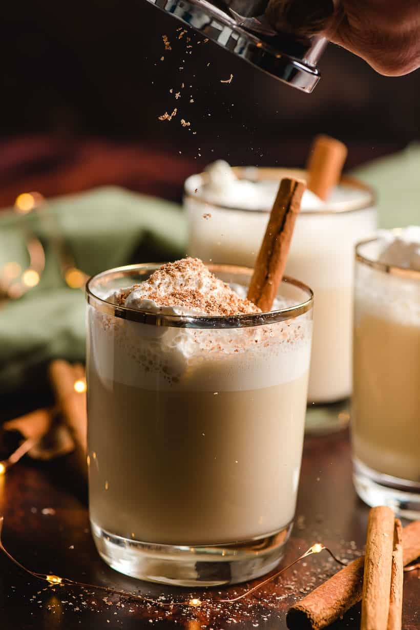 nutmeg being grated onto a glass of eggnog