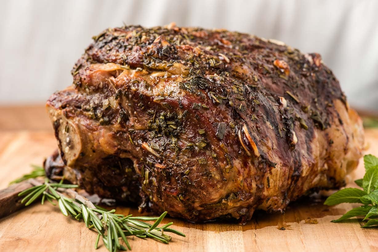 a roasted lamb leg on a carving board with herbs
