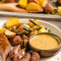 plate filled with baked italian sausage link, dipping sauce, and roasted vegetables