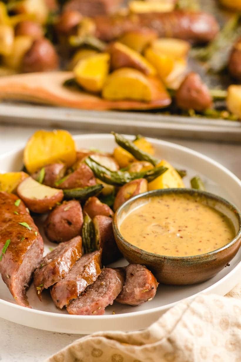 plate filled with baked italian sausage link, dipping sauce, and roasted vegetables