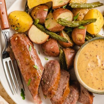 Sliced Italian sausage and potatoes on a plate with dipping sauce.