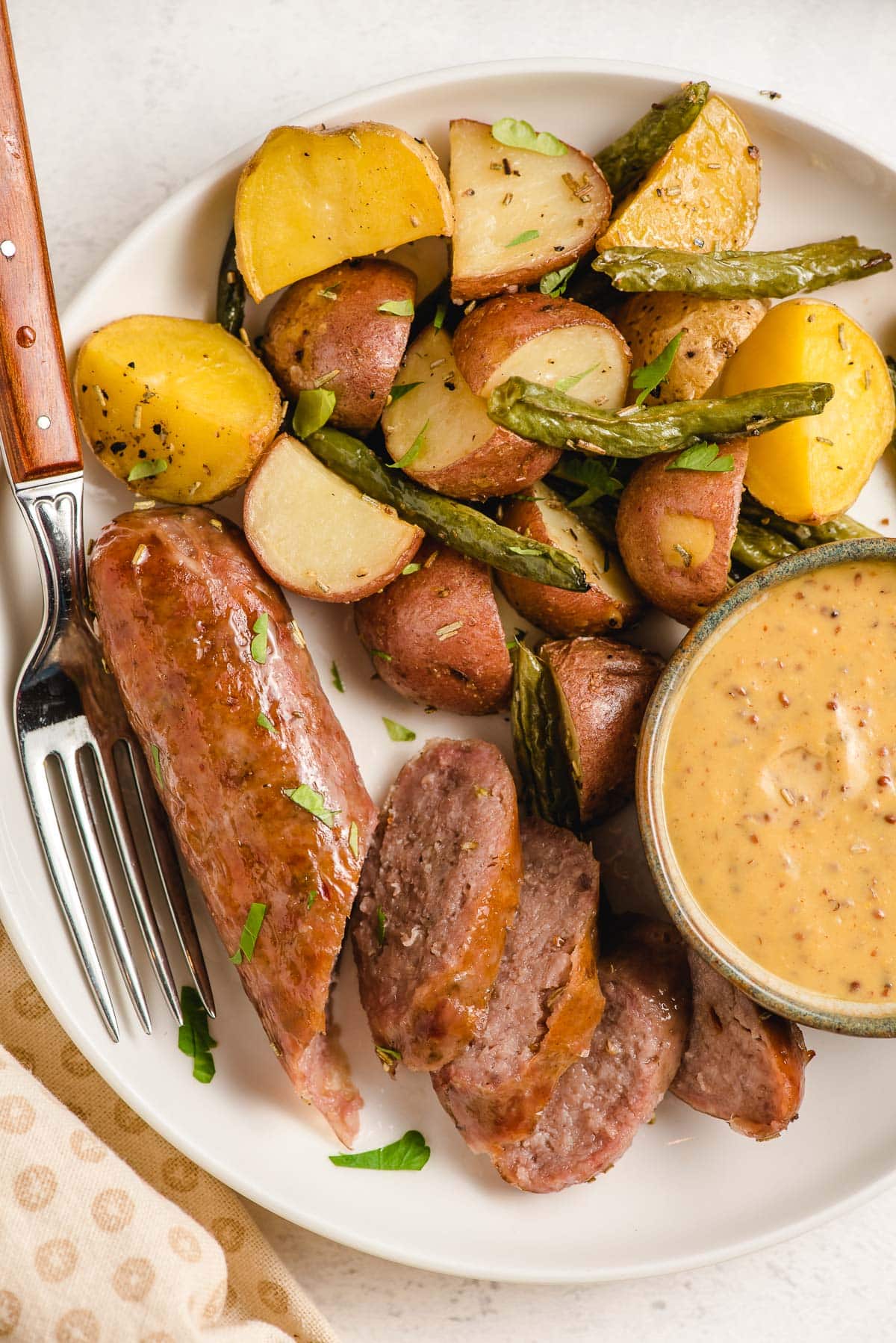 Sliced Italian sausage and potatoes on a plate with dipping sauce.