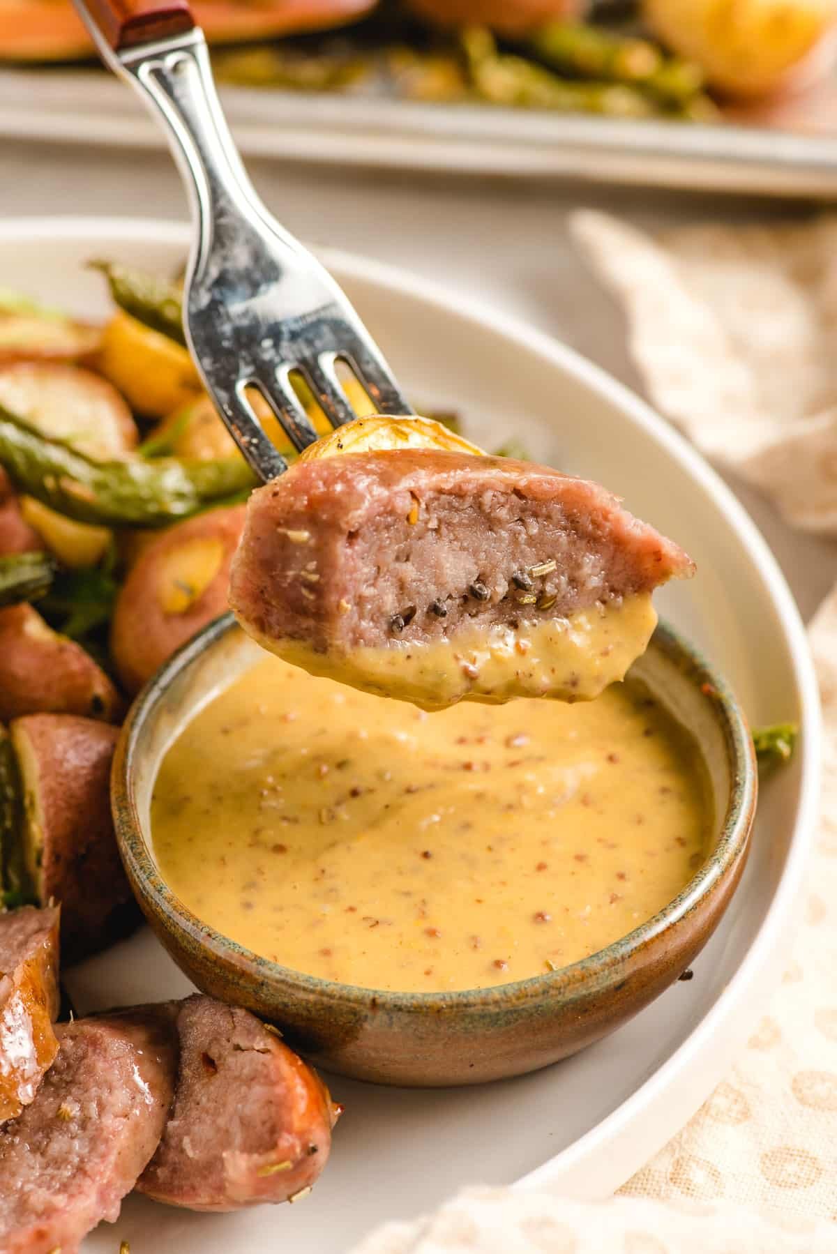 Fork stabbing a slice of Italian sausage dipped in mustard sauce.
