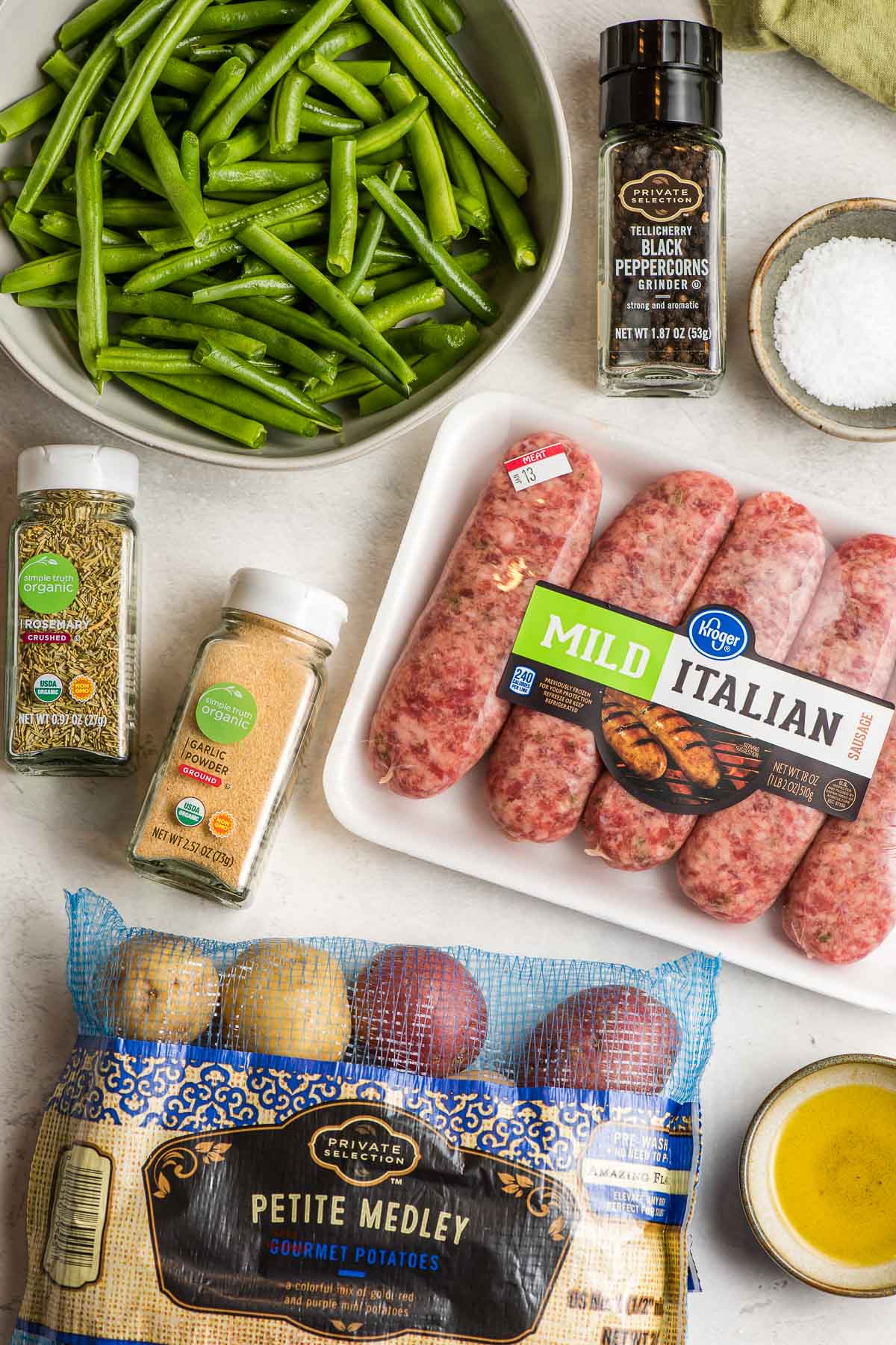 Italian sausage, green beans, baby potatoes, garlic powder, dried rosemary, pepper, salt, and olive oil shown on a white background.