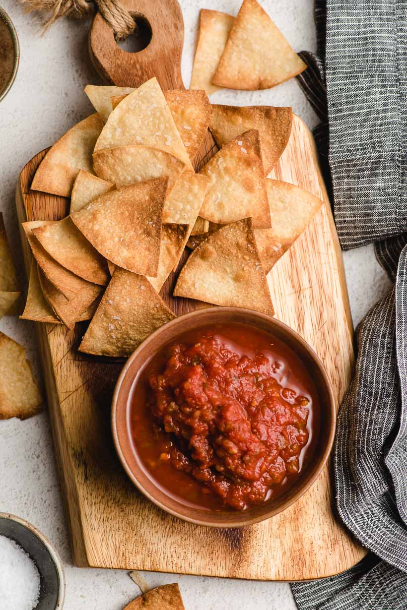 Homemade tortilla chips on a cutting board with a bowl of salsa.