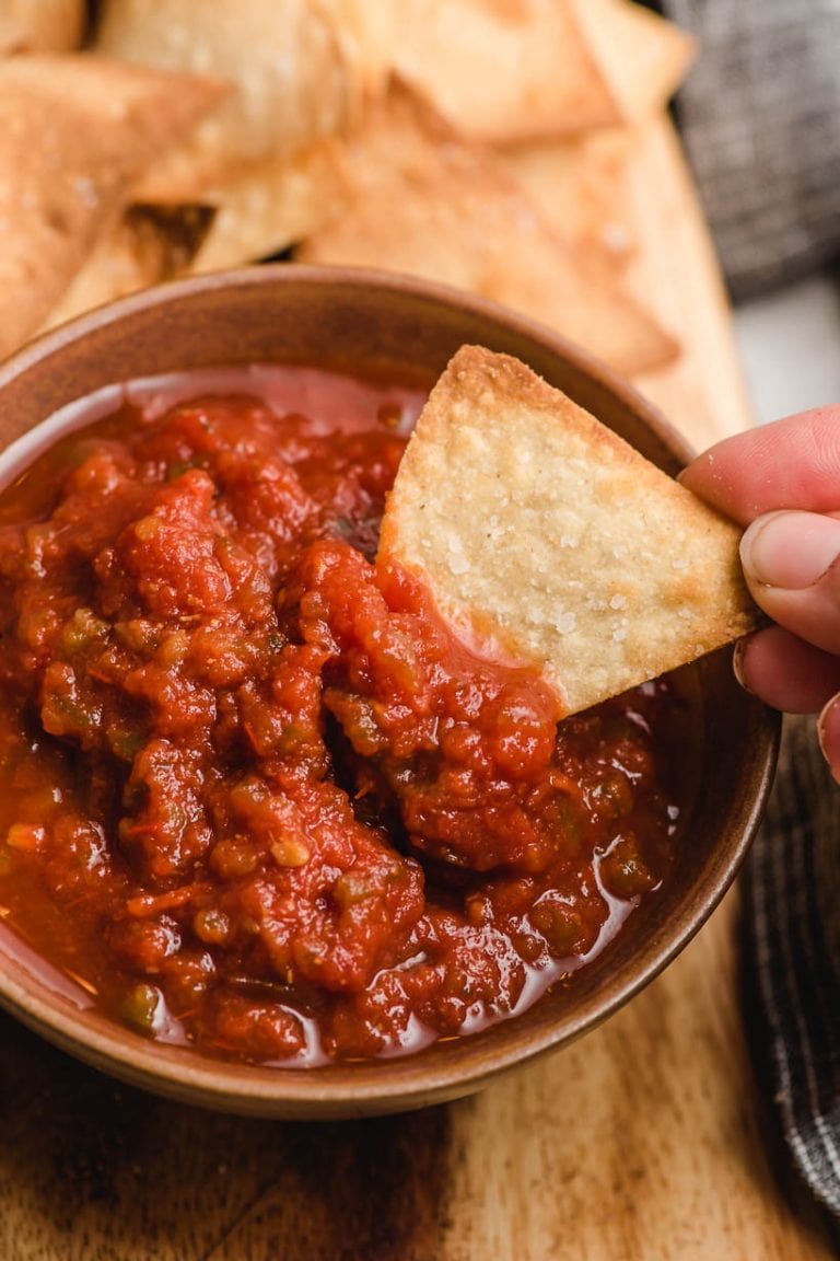 Hand grasping a tortilla chip dipping into a bowl of salsa.