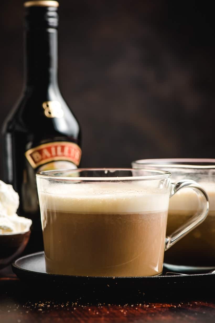 Glass mug filled with Irish Coffee with bottle of Bailey's Irish Cream in the background.