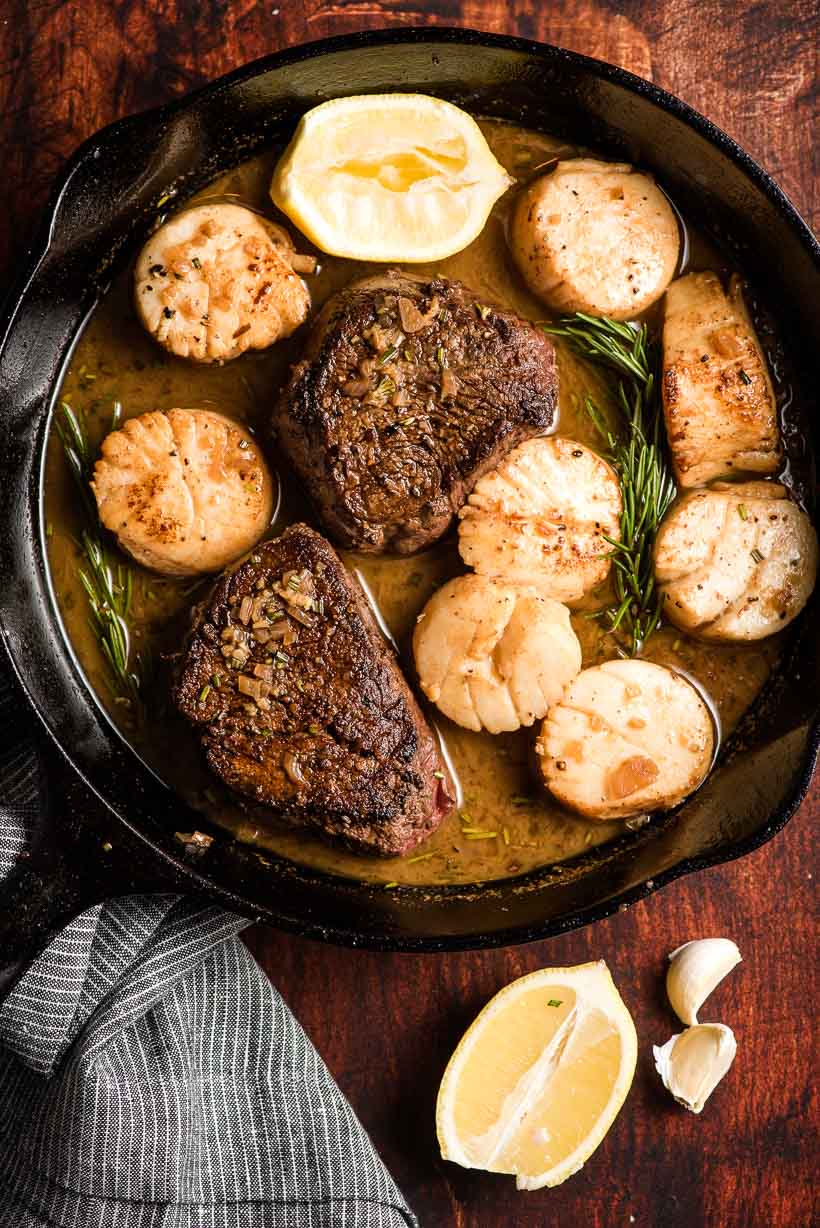 Two filet mignon steaks and sea scallops in a skillet with white wine pan sauce.