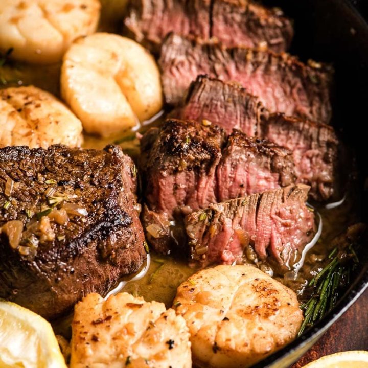 Sliced steak with pink center in a skillet with scallops.