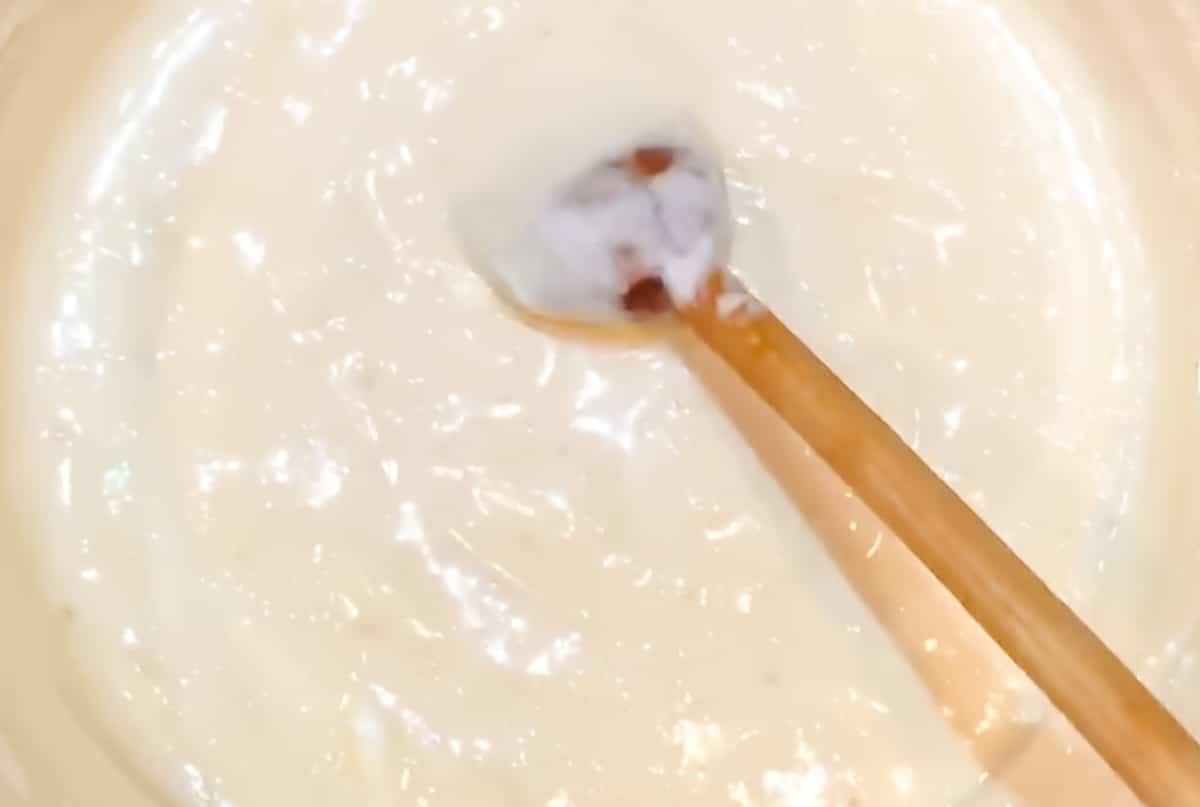 Wooden spoon stirring marshmallows melted into butter and sweetened condensed milk in a pot.