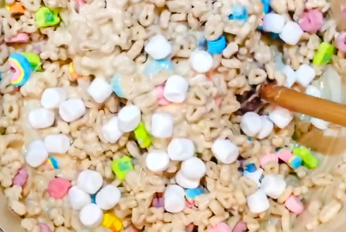 Mini marshmallows being stirred into Lucky Charms and melted marshmallows.