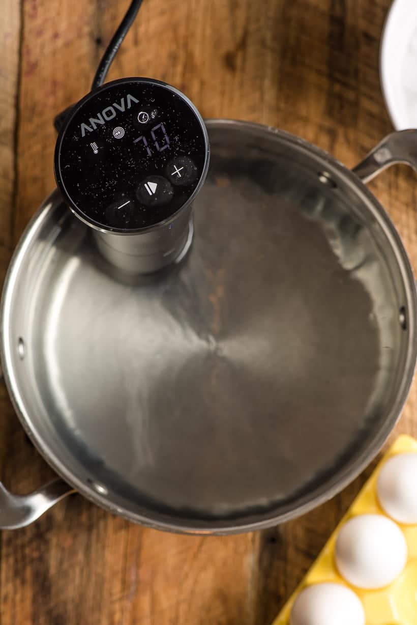 A sous vide immersion cooker sits in a stock pot of water about to cook eggs.
