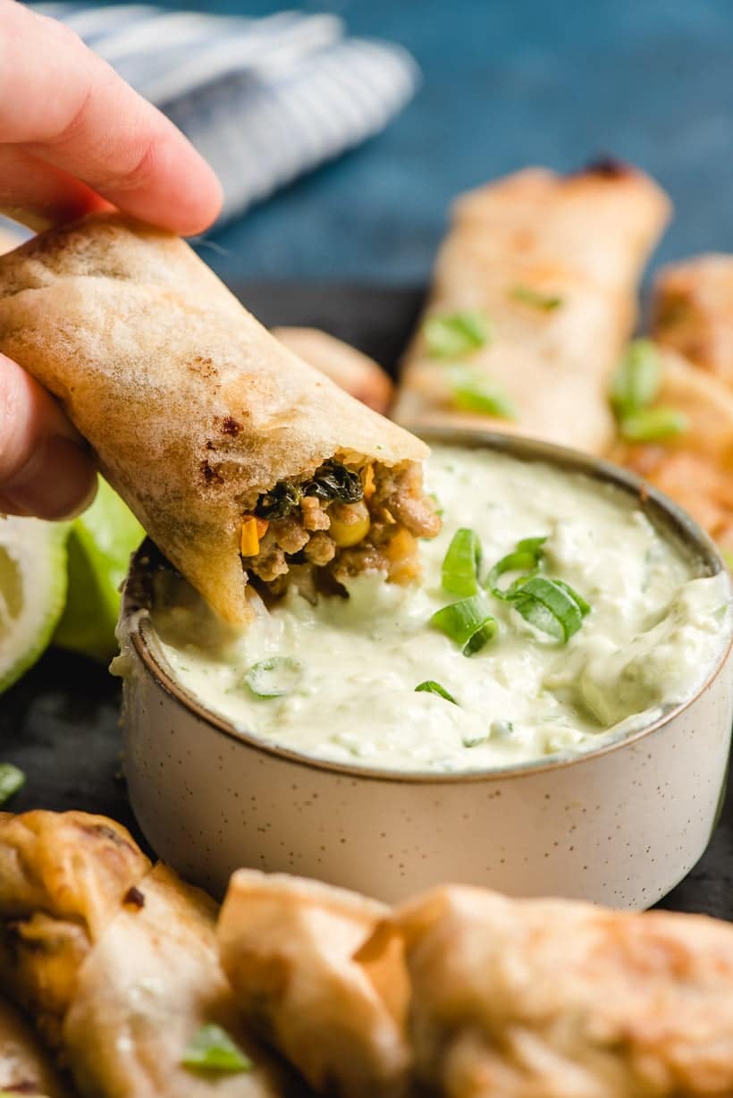 An Southwest Air Fryer Egg Roll with a bite taken out of it dips into a bowl of avocado lime dip. 