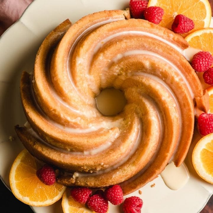 Top down image of a swirled orange bundt cake with orange slices and raspberries.