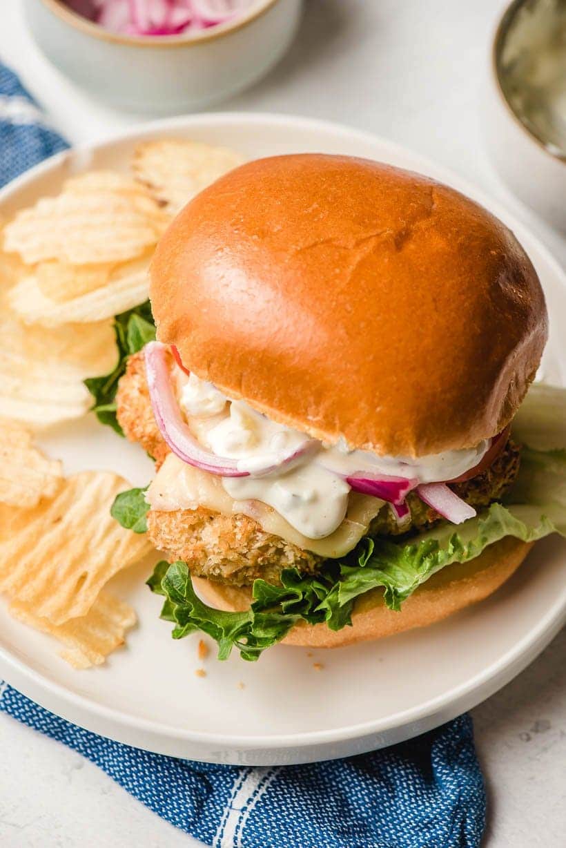 Cod Fish Sandwich on a white plate with potato chips on the side.