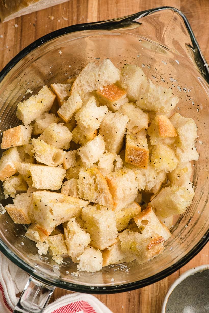 Large glass bowl filled with seasoned bread cubes.