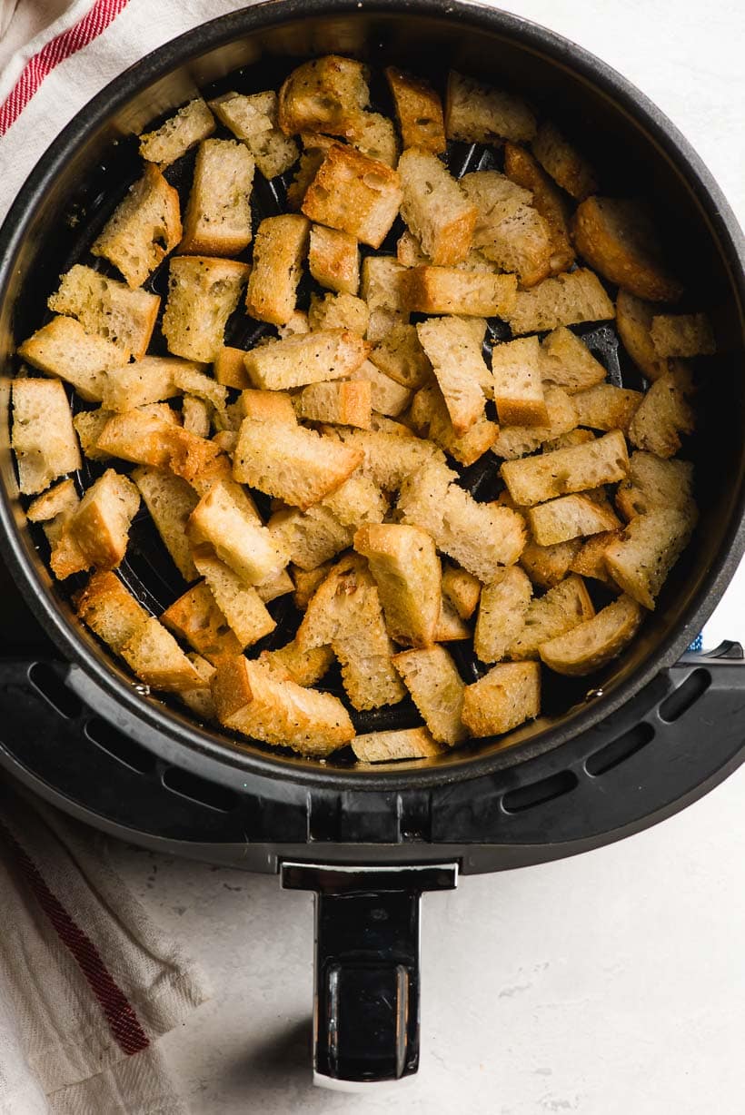 Air fryer basket filled with crunchy fried croutons.