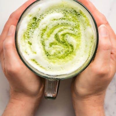 Hands holding a hot matcha latte.