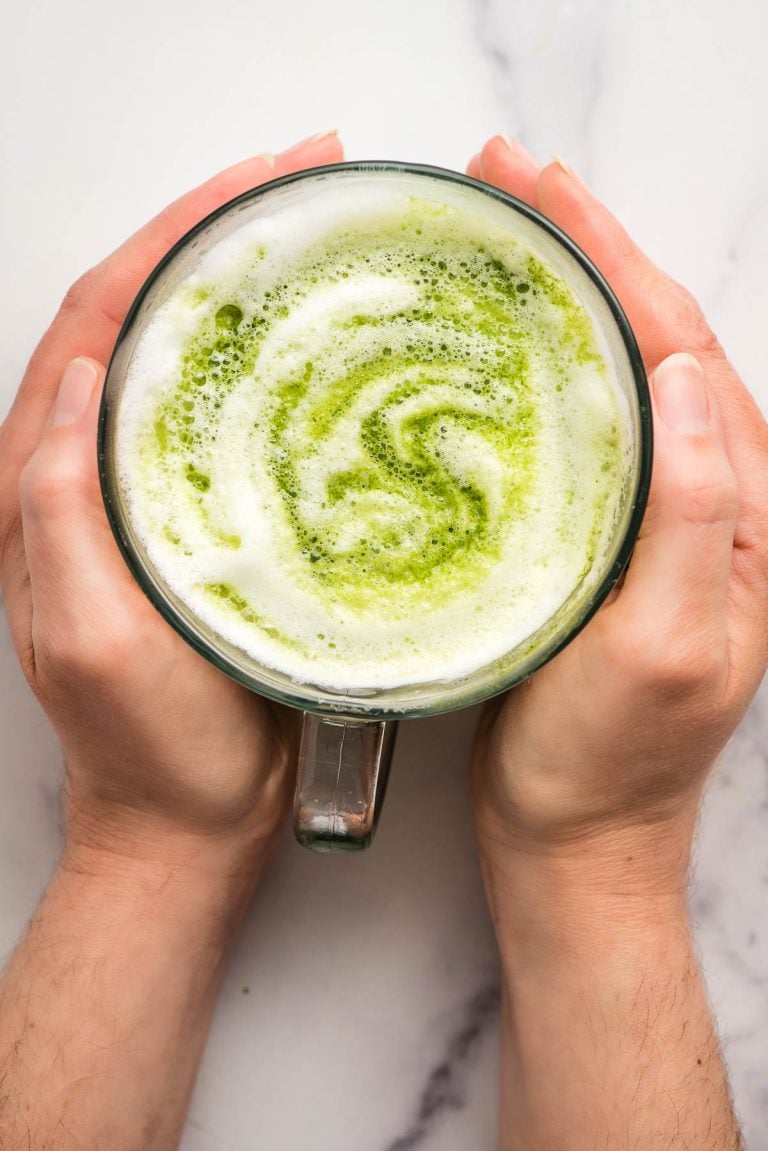 Hands holding a hot matcha latte.