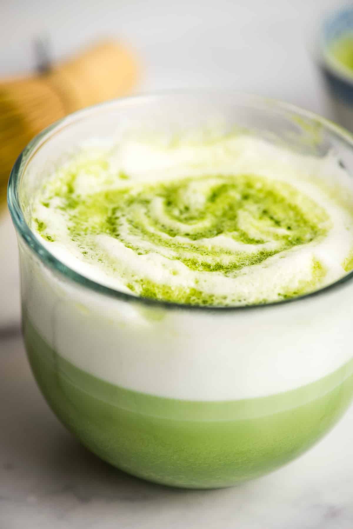 a hot Matcha latte topped with frother milk in a glass mug.
