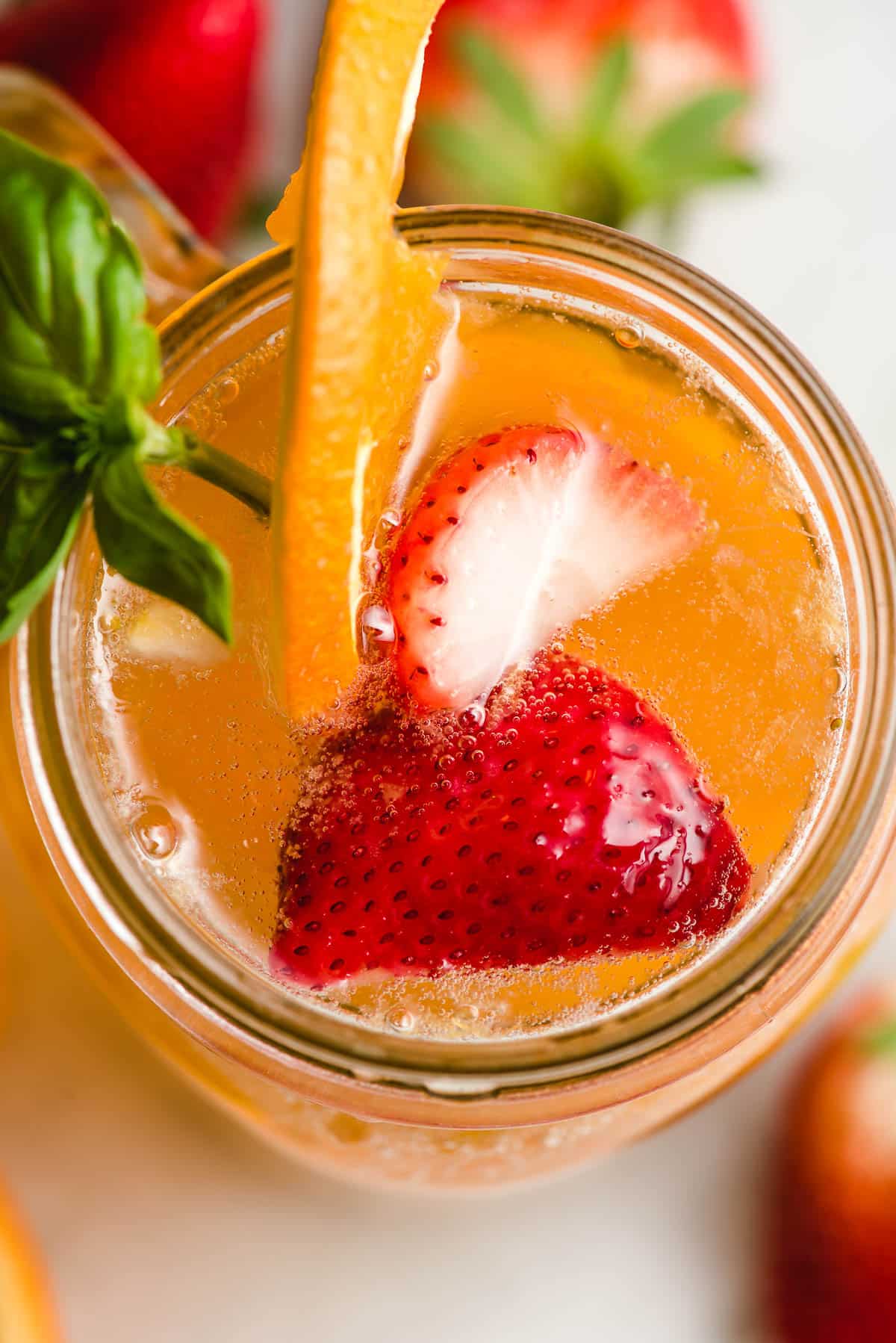 Bubbly white sangria glass with strawberry slices, orange slices, and fresh basil.