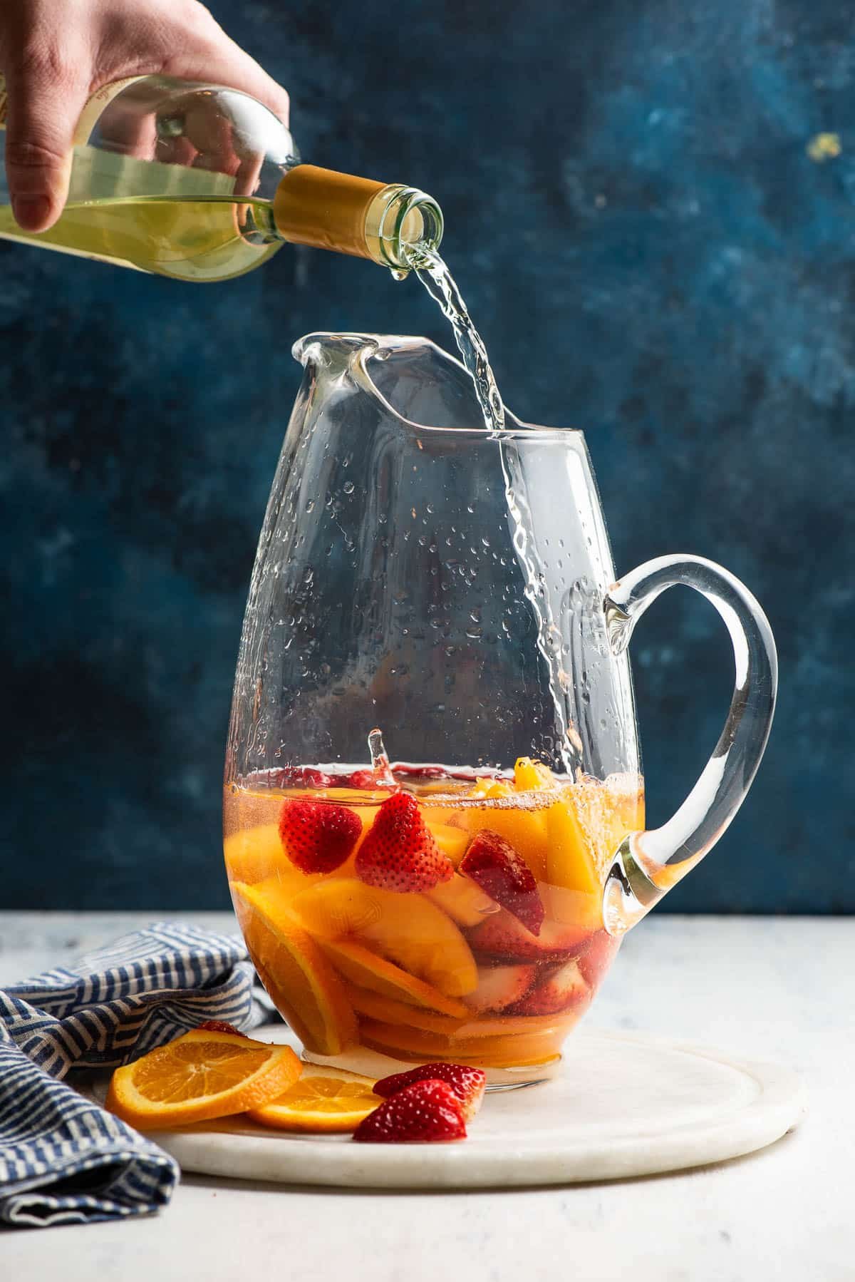 Wine being poured into a glass pitcher with peaches, strawberries, and orange slices.