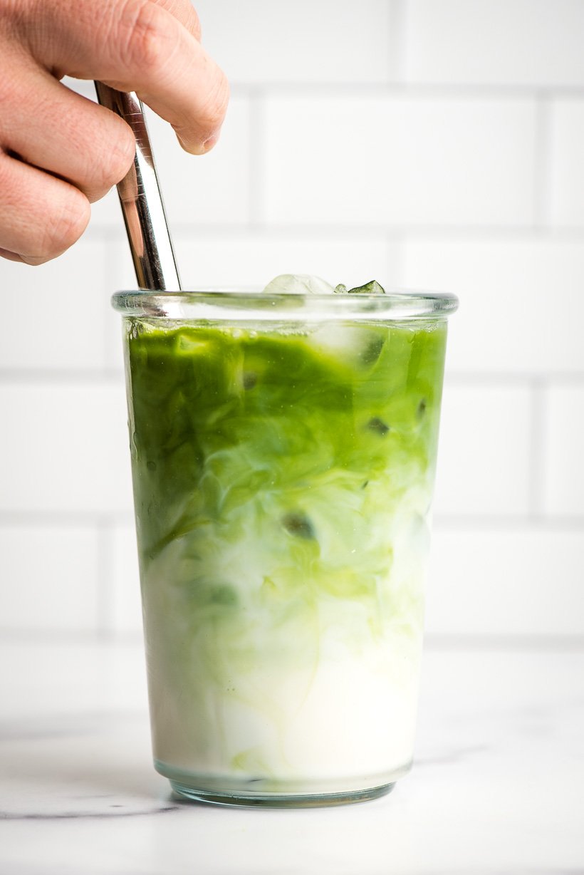 Hand using a straw to swirl matcha into a glass of cold milk.