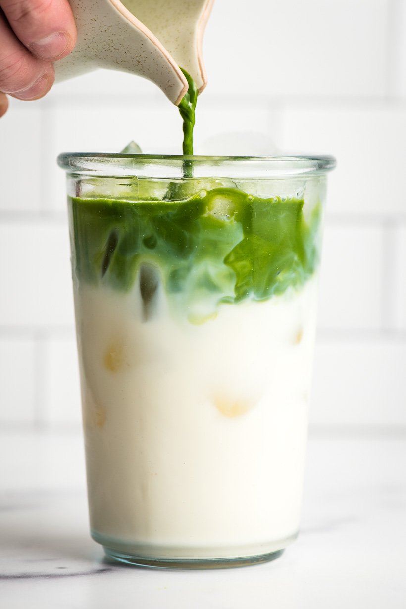 Small pitcher pouring matcha tea into a glass of cold milk.