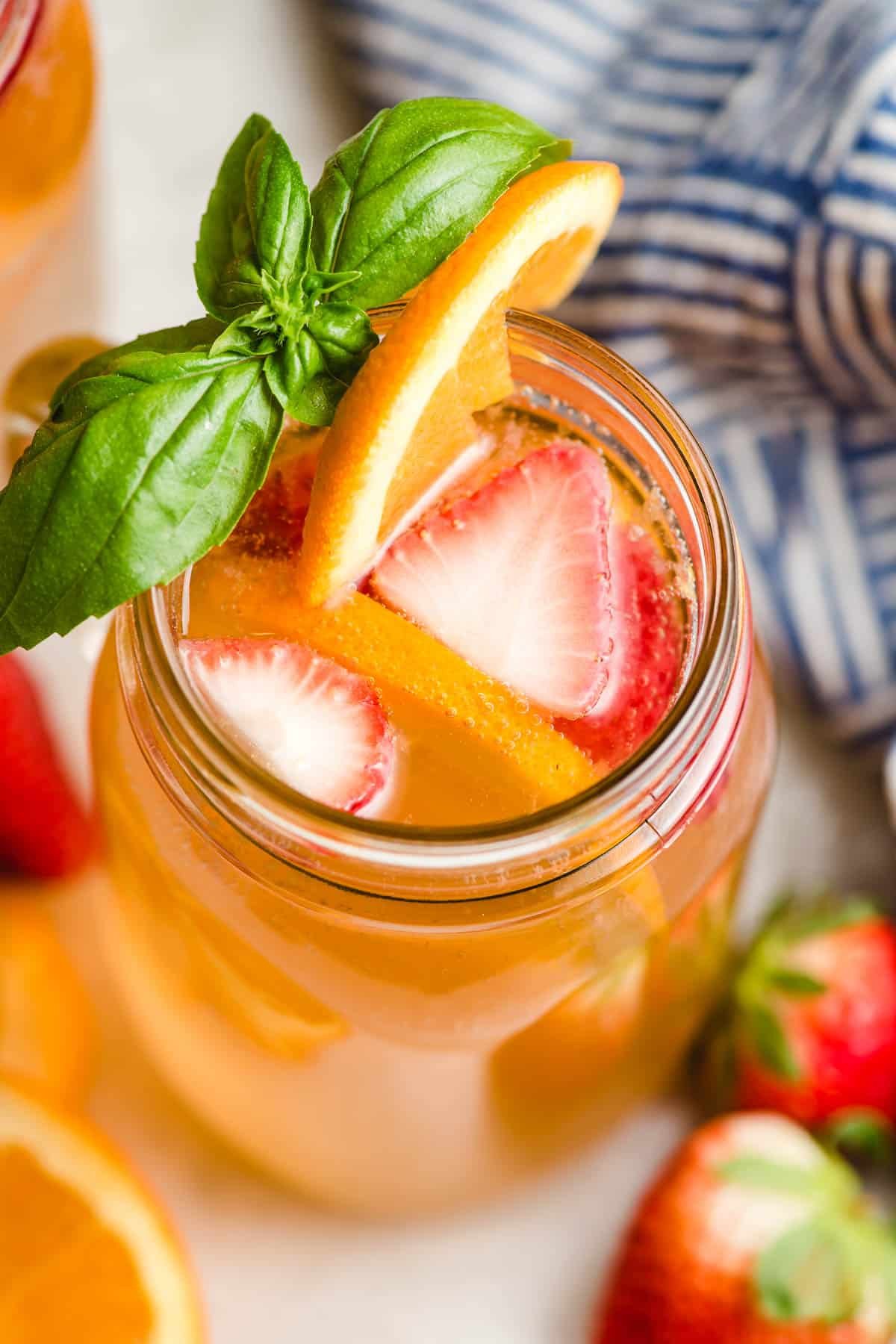 Glass of white sangria with fresh basil sprig, strawberries, and orange garnish.