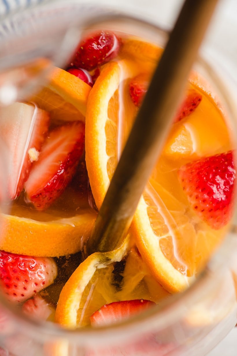 Top down image of a pitcher filled with oranges, peaches, strawberries, sugar, and white wine.
