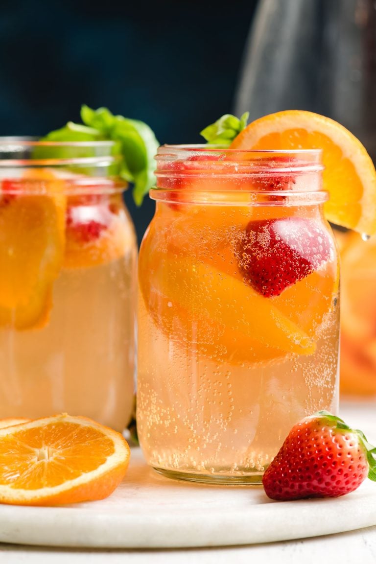 White wine sangria with peaches and strawberries in a glass drinking mug.