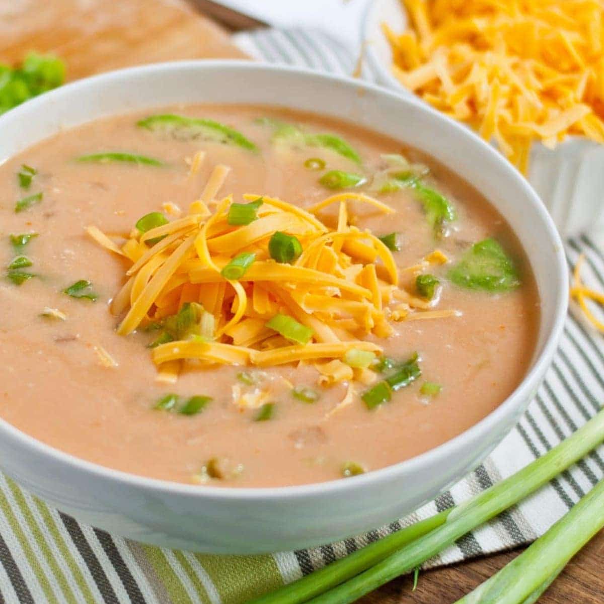 Buffalo Chicken Soup in a white bowl, garnished with shredded cheddar cheese and sliced green onions.