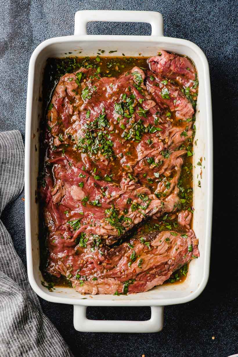 Skirt steak covered in a soy sauce marinade in a white casserole dish.