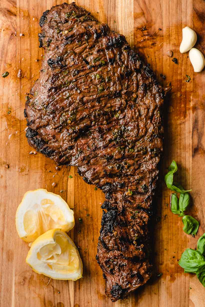 Grilled skirt steak on a wooden cutting board with lemon wedges.