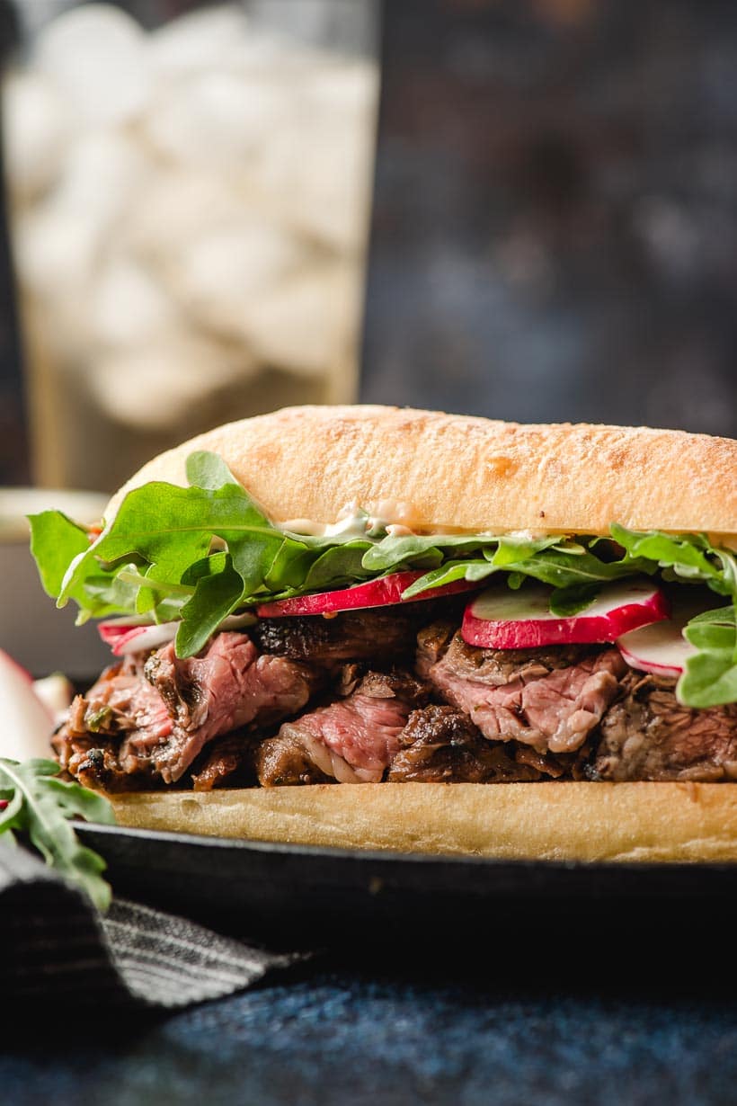 Steak sandwich on a ciabatta roll topped with arugula and sliced radishes.
